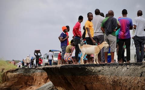 Locals stand beside a damaged section of the road between Beira and Chimoio in Nhamatanda district, central Mozambique - Credit: AFP