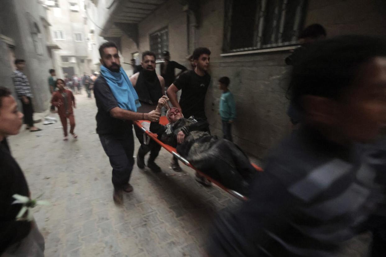 People in dark clothing carry a woman on a stretcher past a building