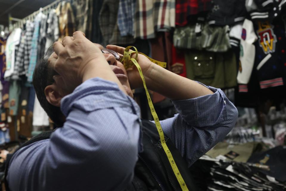 A man holding a tape measure puts his hands to his head and his face toward the ceiling.