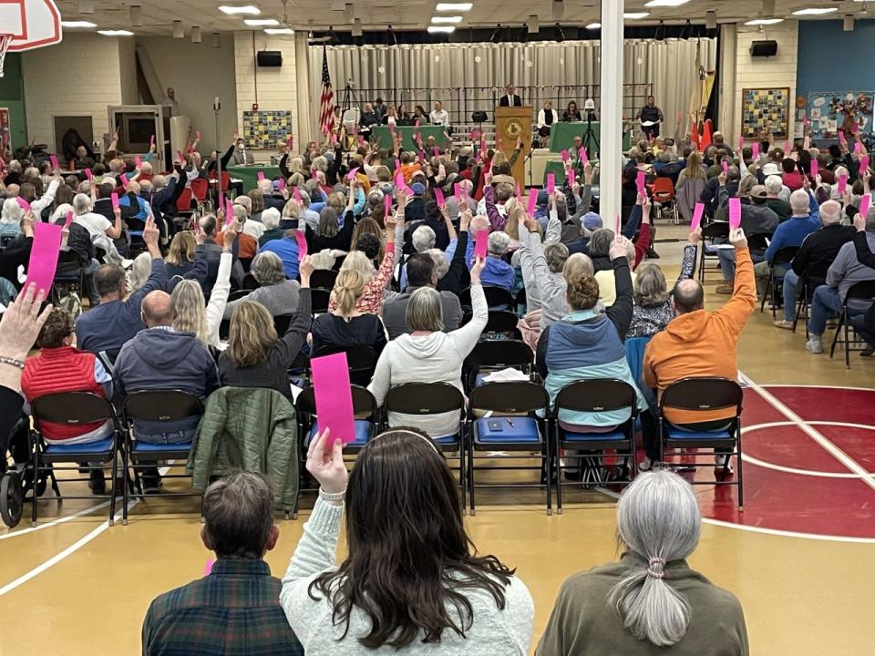 Voters at Brewster's annual town meeting on Monday raise their cards in support of an override to fully fund the Nauset Regional School District budget.