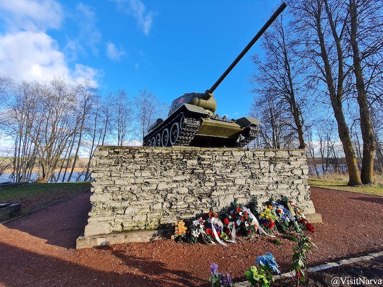 Tank on a plinth of stones with bouquets on the ground in front