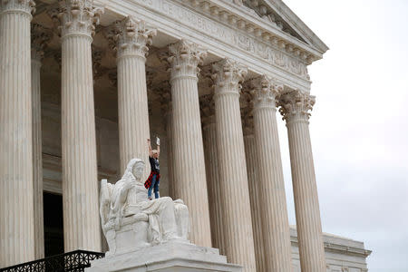 A protester stands on the lap of "Lady Justice" on the steps of the U.S. Supreme Court building as demonstrators storm the steps and doors of the Supreme Court while Judge Brett Kavanaugh is being sworn in as an Associate Justice of the court inside on Capitol Hill in Washington, U.S., October 6, 2018. REUTERS/Carlos Barria