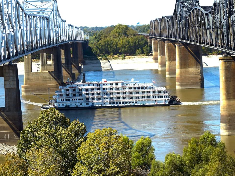 paddlewheel boat full of windows passes between two bridges with low water on mississippi river