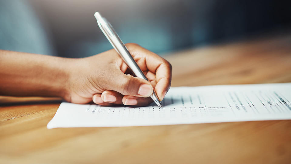 Cropped shot of a woman filling in some paperwork at a desk.