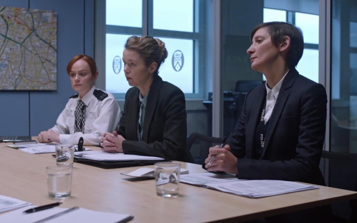 Three actors are shown sitting at a table together, one in police uniform