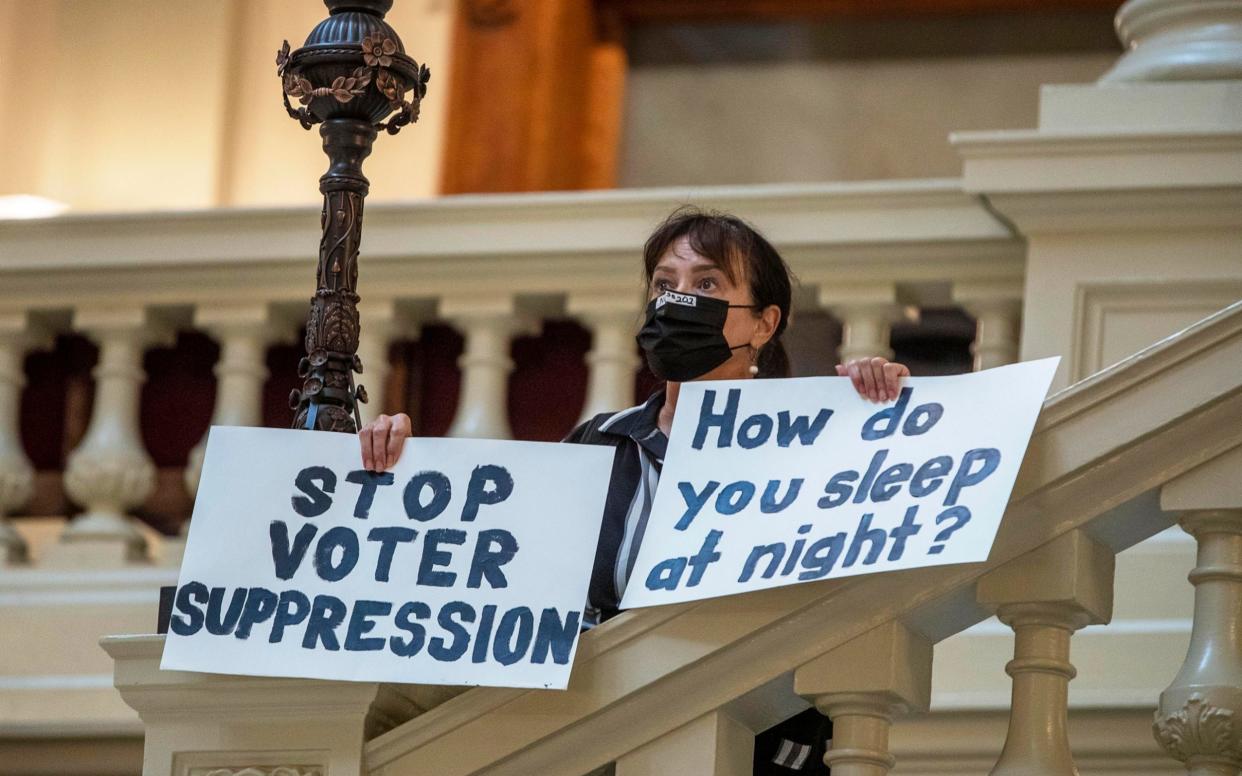 Protester holds up a sign on the steps Georgia State Capitol as new voter law is passed - AP