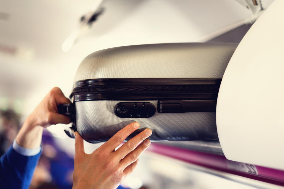 Person placing a carry-on suitcase into an overhead bin on an airplane