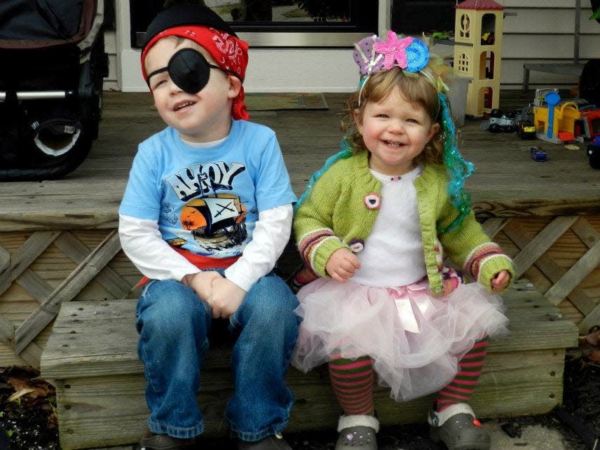 Two children dressed for Halloween. The child on the left is dressed as a pirate and the younger child on the right wears a green cardigan, with a glittery headband, pink tutu and red and green striped leggings.