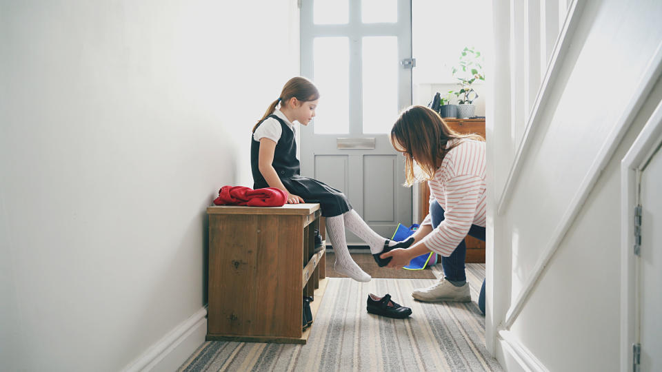 mother kneeling on the floor to help school-age daughter to put on her school shoes