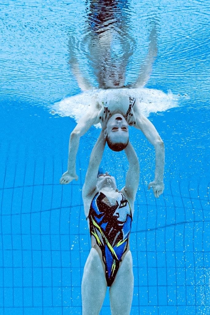 A swimmer pushing her teammate out of the water