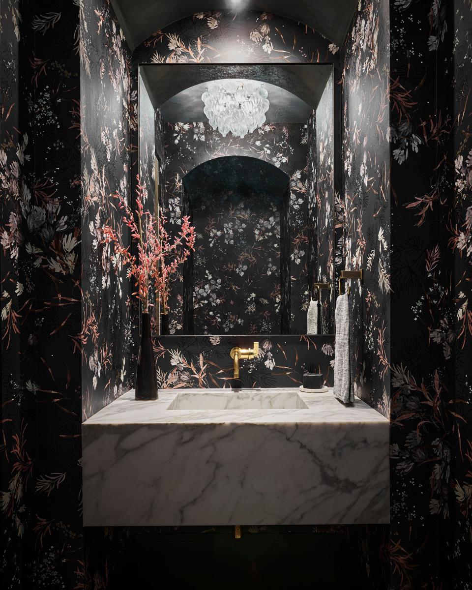 A dark flowered Kelly Ventura wallpaper lines this powder room, which features a custom Calacatta marble sink and a custom iron-framed mirror from Mirror-tique.