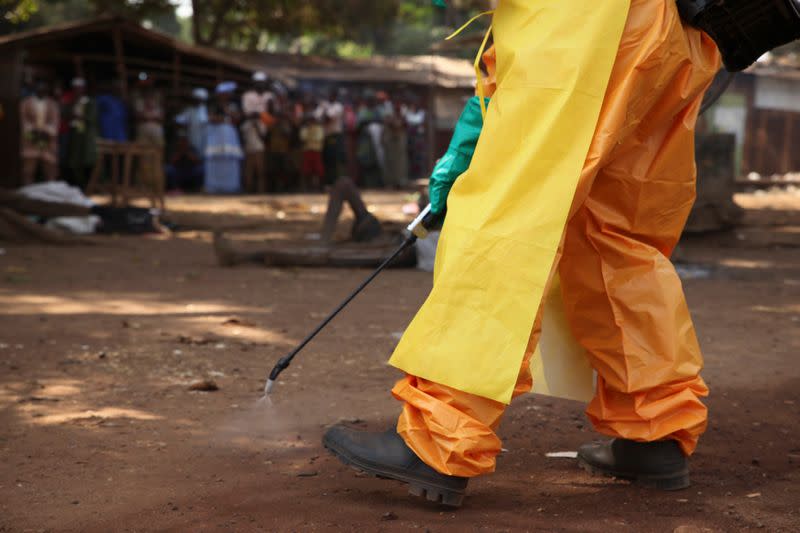 A member of the French Red Cross disinfects the area around a motionless person suspected of carrying the Ebola virus as a crowd gathers in Forecariah