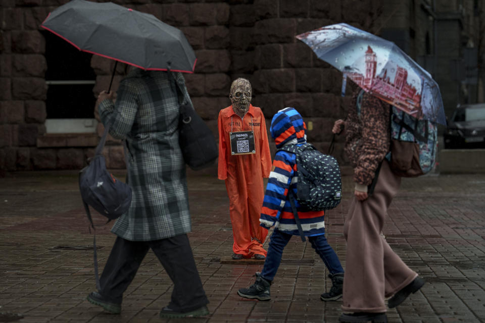 People walk by an effigy of Russian President Vladimir Putin dressed in a prisoner outfit during a rainfall in Kyiv, Ukraine, Monday, March 18, 2024. President Vladimir Putin secured a fifth term after the harshest clampdown on the opposition and free speech in the country since the Soviet era. (AP Photo/Vadim Ghirda)