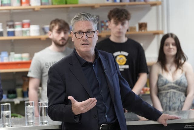 Sir Keir Starmer stands in front of three students