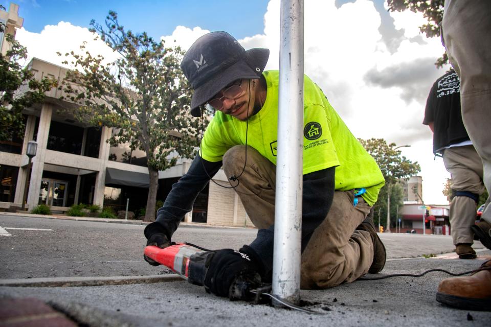 D'Angelo Hernandez, 19, with the San Joaquin Office of Education's Greater Valley Conservation Corps (GVCC) uses a saw as a part of crew to remove old parking meter posts on Market Street between Center and El Dorado streets in downtown Stockton, April 22.