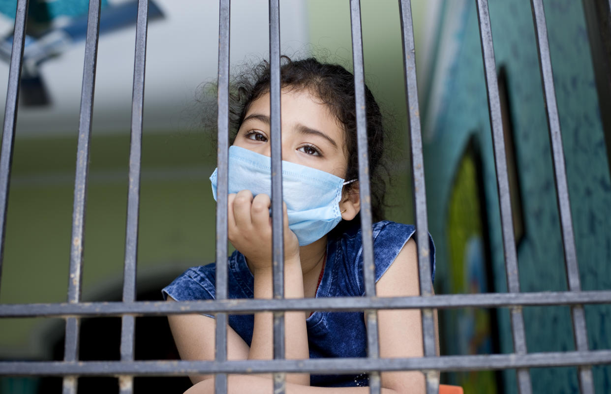 Little girl wearing a face mask and peeking out from window