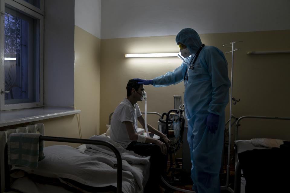 In this photo taken on Tuesday, April 28, 2020, a doctor, wearing a special suit to protect against coronavirus, speaks to a patient with coronavirus during evening examination at a hospital in Malyn, Ukraine. Ukraine's troubled health care system has been overwhelmed by COVID-19, even though it has reported a relatively low number of cases. (AP Photo/Evgeniy Maloletka)