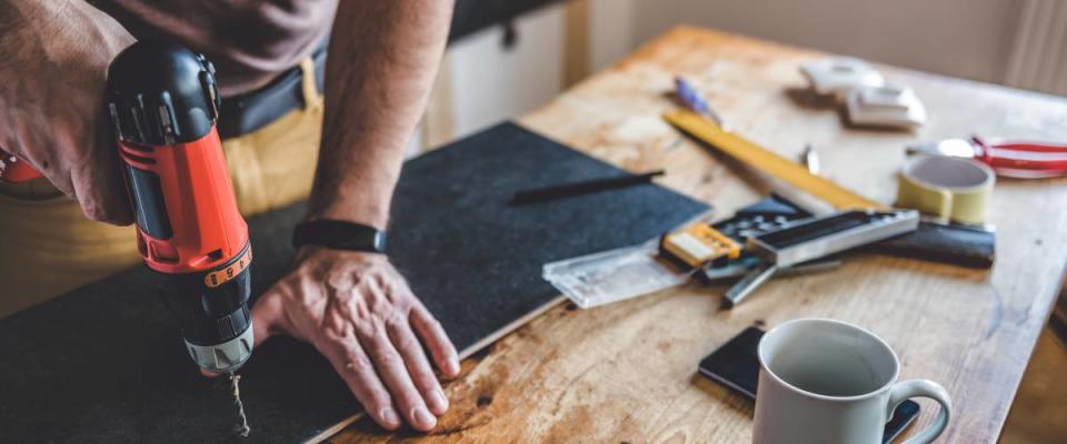 Man uses a drill on a piece of wood sitting on a table.