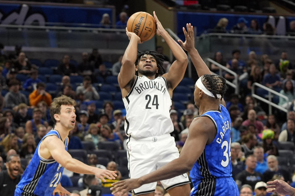 Brooklyn Nets guard Cam Thomas (24) shoots from between Orlando Magic forward Franz Wagner, left, and center Wendell Carter Jr. during the first half of an NBA basketball game Wednesday, March 13, 2024, in Orlando, Fla. (AP Photo/John Raoux)