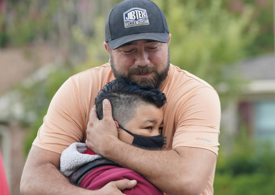 Russell Rakestraw II hugs his son fourth grader Russell Rakestraw III in front of his elementary school while dropping off on the first day of classes in Richardson, Texas, Tuesday, Aug. 17, 2021. Despite Texas Gov Greg Abbott's executive order banning mask mandates by local officials, the Richardson Independent School District and many others across the state are requiring masks for students. (AP Photo/LM Otero)