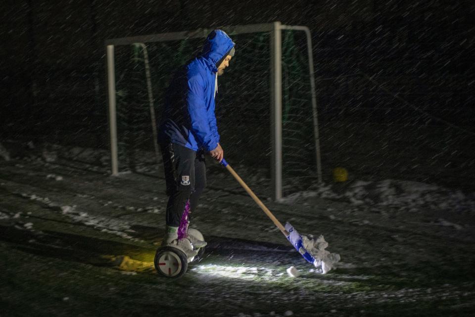 A man rides his hoverboard as he clears snow from a pitch ahead of a soccer game in Irpin, Kyiv region, Ukraine, Tuesday, Nov. 29, 2022.