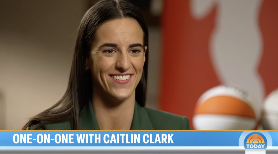 Caitlin Clark in an interview, smiling, wearing a green blazer with basketballs in background, text "ONE-ON-ONE WITH CAITLIN CLARK" below