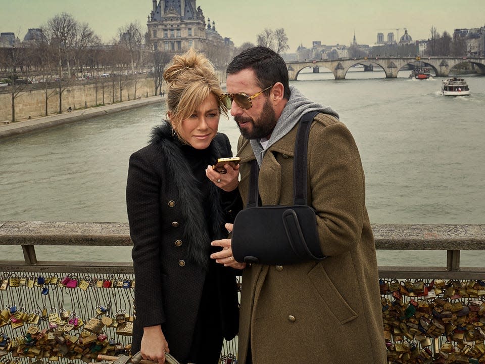 Jennifer Aniston and Adam Sandler speaking on a phone on a bridge