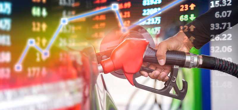 A hand holding a fuel nozzle with a market data chart in the background.