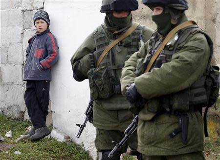 A boy looks at uniformed men, believed to be Russian servicemen, near a Ukrainian military base in the village of Perevalnoye, outside Simferopol, March 6, 2014. REUTERS/Vasily Fedosenko