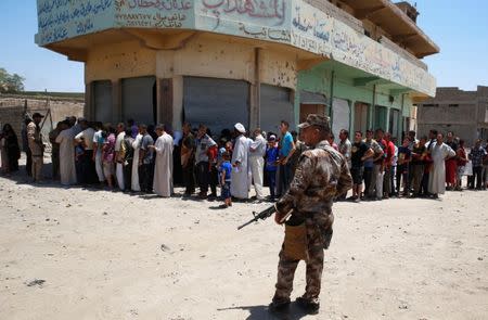 An Iraqi soldier stands guard as displaced Iraqi residents queue for a food distribution by an aid organization during the first day of Eid-al Fitr celebration in West Mosul, Iraq June 25, 2017. REUTERS/Erik De Castro