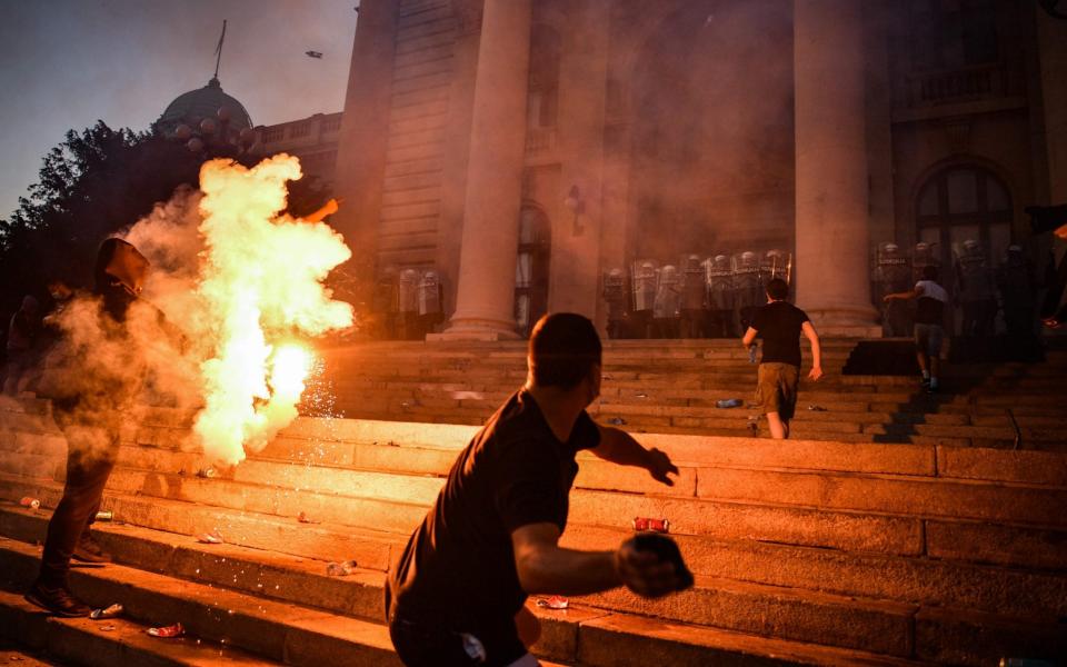 A protester prepares to throw a missile at police guarding Serbia's parliament on Wednesday as Belgrade was hit by a second night of rioting over a proposed renewed lockdown  - ANDREJ ISAKOVIC/AFP