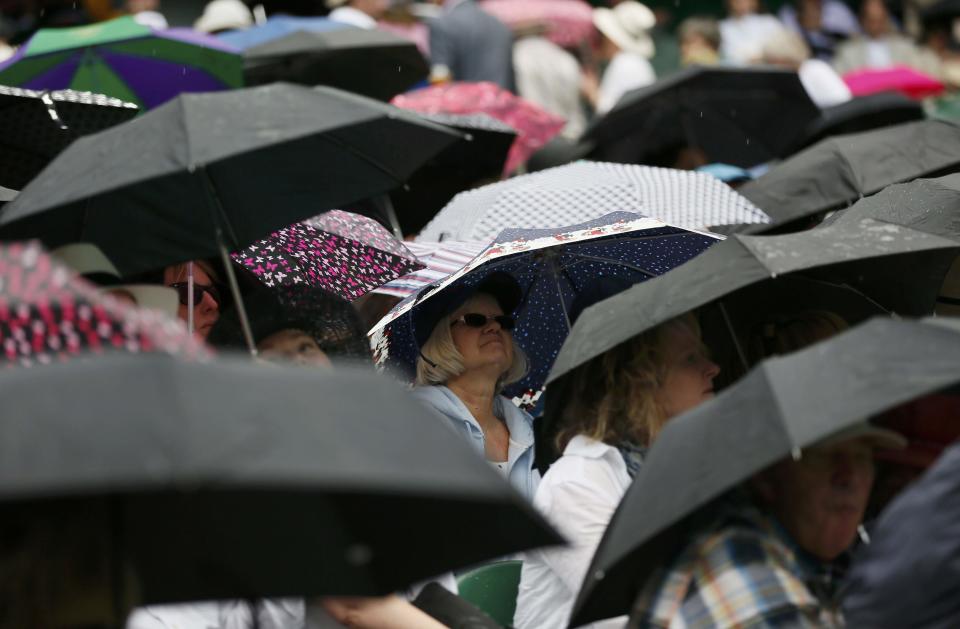 Spectators put umbrellas up during a rain delay on Centre Court at the Wimbledon Tennis Championships in London