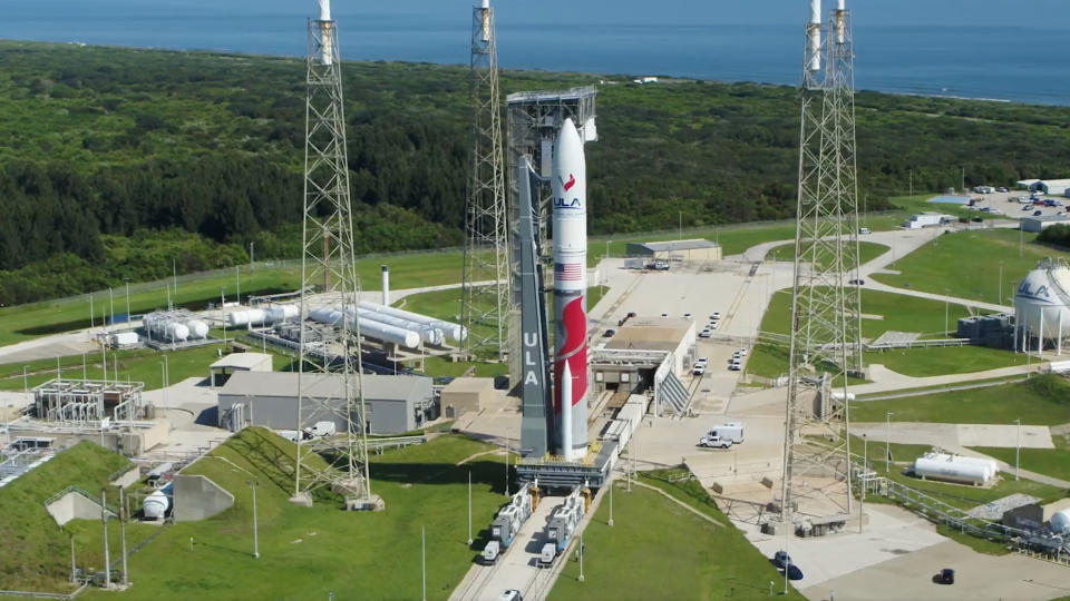     Luftaufnahme einer rot-weißen Rakete auf der Startrampe, mit Grün und dem Meer im Hintergrund. 