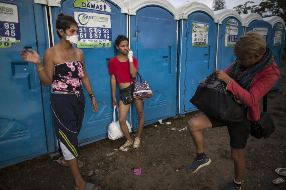 In this Nov. 1, 2018 photo, Valentina Guerrero, of El Salvador, right, and Sinai Cortez, from Nicaragua, center, part of about 50 LGBTQ migrants who are traveling with the caravan hoping to reach the U.S. border, wait their turn to use a portable toilet at a temporary shelter in Donaji, Mexico. Fearful of being attacked violently or sexually assaulted, they've stuck by each other's side 24 hours a day, even using the buddy system for going to the bathroom. (AP Photo/Rodrigo Abd)