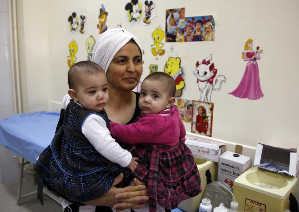 Woman carrying twin girls waits before they receive polio vaccinations at a medical centre in Damascus