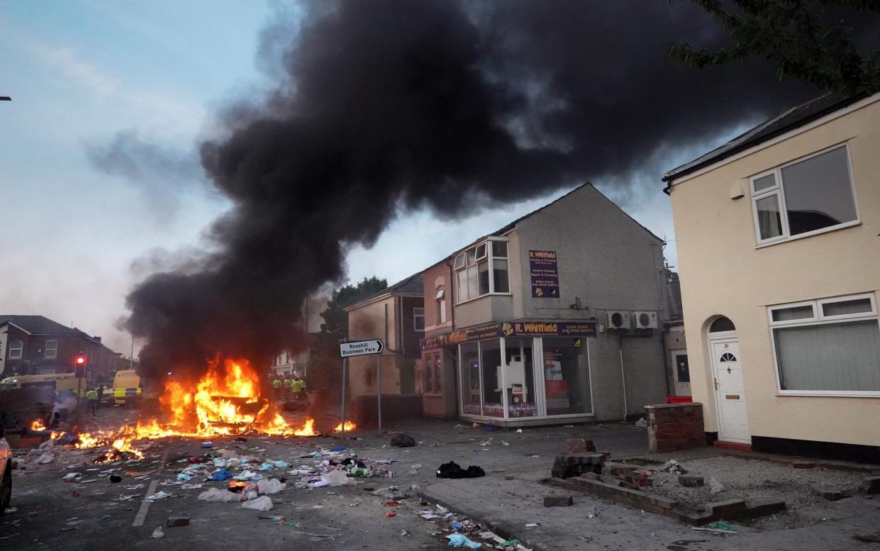 Riot police hold back protesters near a burning police vehicle