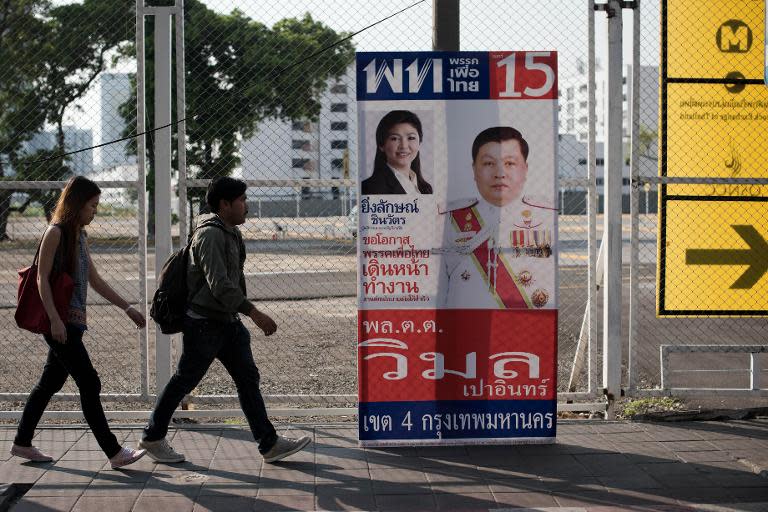 People walk past Thai Prime Minister Yingluck Shinawatra's election campaign poster in Bangkok on January 31, 2014