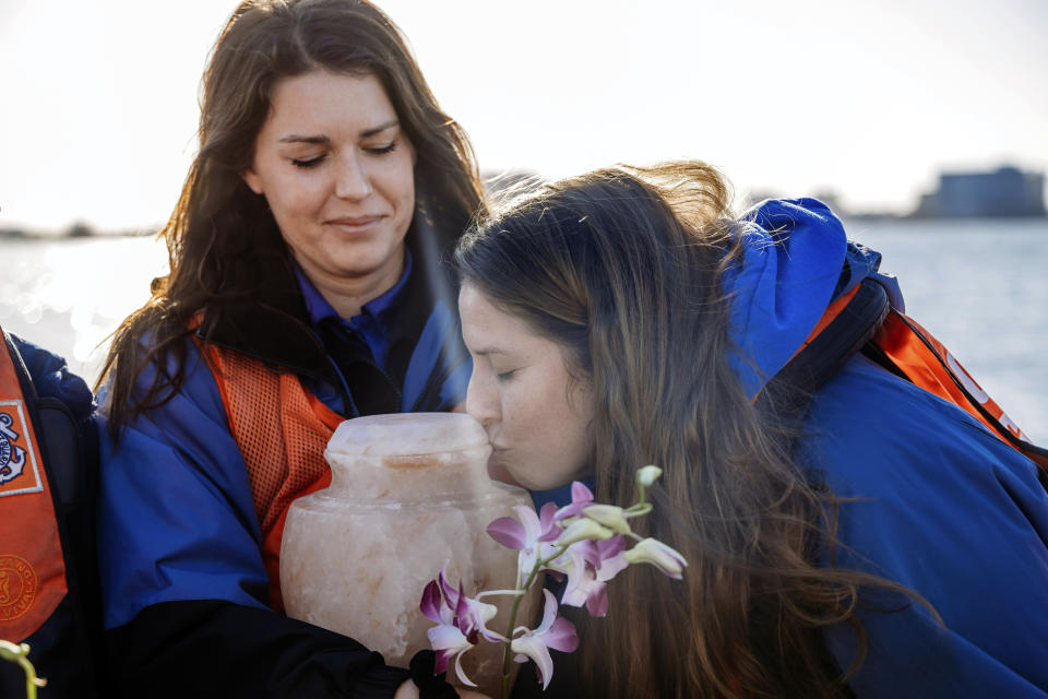Clearwater Marine Aquarium animal care specialist Kaylee Rhieu, right, kisses the urn with the ashes of Winter the Dolphin, held by animal care specialist Allison Twedt, as aquarium staff members prepared to the release them into the Gulf of Mexico from the back of a U.S. Coast Guard response boat, Thursday, Jan. 13, 2022, of the coast of Clearwater, Fla. Winter, a prosthetic-tailed dolphin that starred in the “Dolphin Tale” movies, died on Nov. 11, 2021, at age 16 of an inoperable intestinal problem. (Clearwater Marine Aquarium via AP)
