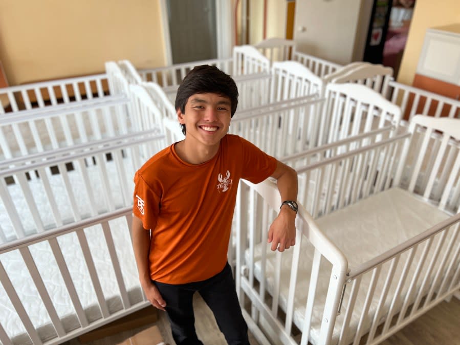 Griffin standing with the cribs he donated (Photo Courtesy: Susan Moore).