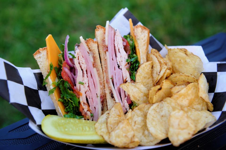 The Club sandwich from Traveler's Deli is stacked with ham and turkey, cheddar and Swiss cheeses, tomato, onion, greens, bacon jam, and aioli on toasted bread.