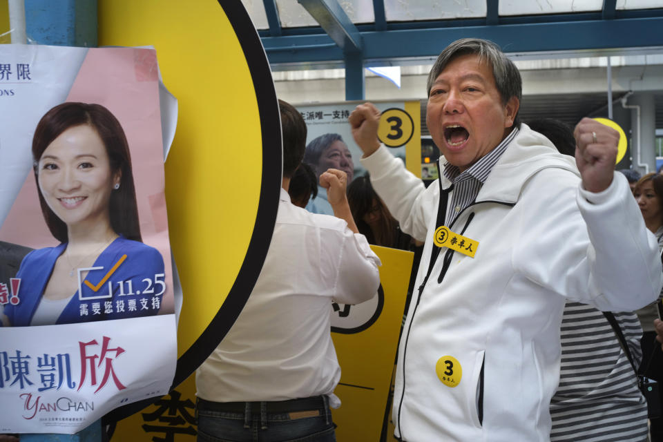 FILE - In this Nov. 25, 2018, file photo, pro-democracy candidate Lee Cheuk-yan shouts slogans next to an election poster of establishment candidate Chan Hoi-yan during a by-election campaign at the voting day in Hong Kong. Hong Kong's Apple Daily newspaper said Friday, Feb. 28, 2020, the vice chairman of the opposition Labor Party, Lee, and others were detained by police in connection with the Aug. 31, 2019, march, (AP Photo/Vincent Yu, File)