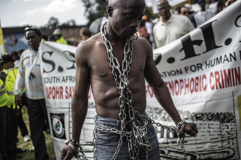 An anti-xenophobia activist stands chained in front of a banner, as thousands of people get ready to march against the recent wave of xenophobic attacks in South Africa through the streets of Johannesburg CBD on April 23, 2015