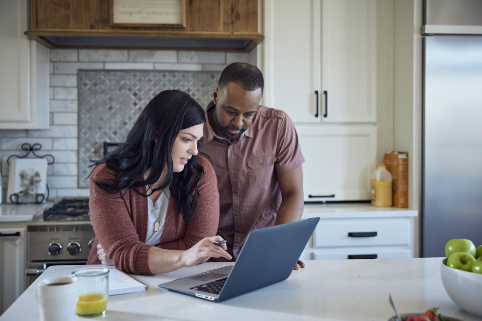 ISA Caucasian woman and African American man sit at kitchen counter with breakfast working with pen, paper and laptop.