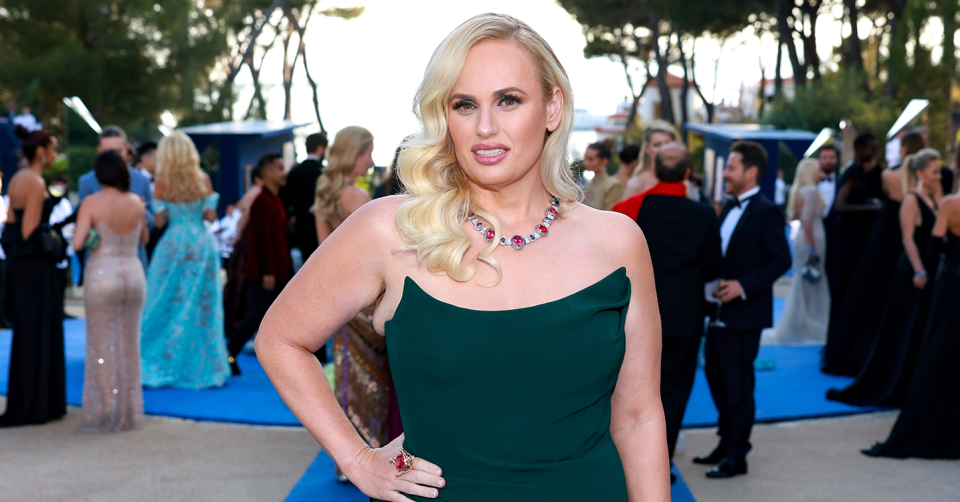 Rebel Wilson poses for a photo with her hand on her hip in a green strapless dress