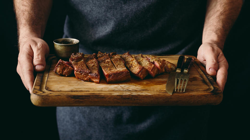 man holding juicy sliced steak cutting board