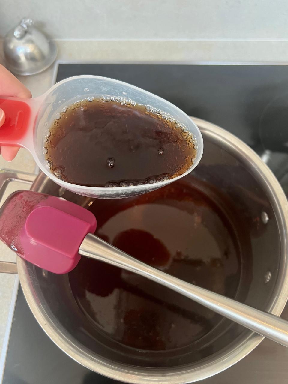 A measuring spoon of Coca-Cola held over a saucepan of brown-coloured batter.