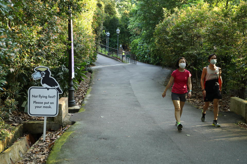 SINGAPORE - 2021/10/09: People wearing face masks as a preventive measure against the spread of covid-19 walk past a sign encouraging the usage of masks at the Botanic Gardens. (Photo by Lionel Ng/SOPA Images/LightRocket via Getty Images)