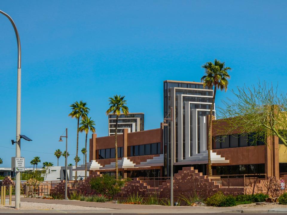 A geometric red, black, and white building with palm trees in front on a day with clear, blue skies