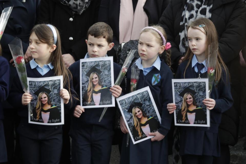 Pupils from Ashling Murphy’s class hold photographs of her and red roses outside St Brigid’s Church, Mountbolus, Co Offaly, for her funeral (PA) (PA Wire)