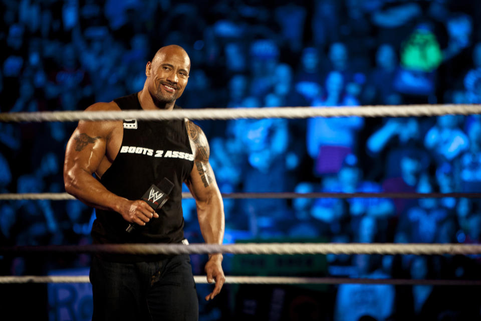 Dwayne Johnson, aka The Rock, holds a microphone in a WWE ring.